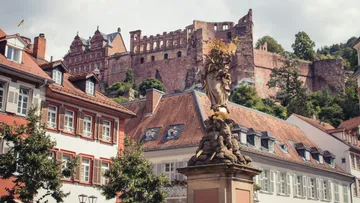 Statue with scepter near old castle and houses.
