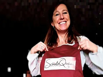 Woman wears apron, smiles and points at logo.