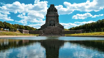 Monument reflecting in a pond, surrounded by trees.