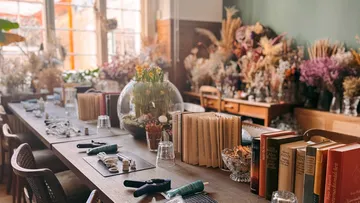 Tisch mit Büchern, Werkzeugen und Trockenblumen.