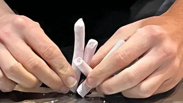Hands shaping clay sticks on table.