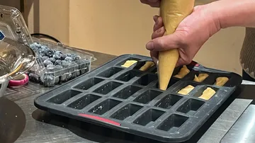 Hand füllt Teig in ein Backblech.