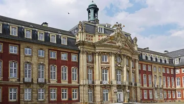 Baroque palace facade with central sculpture, cloudy sky.