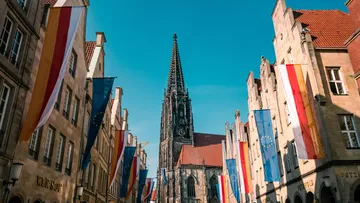 Gotischer Kirchturm umgeben von flaggengeschmückten Gebäuden.
