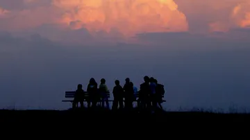 Silhouetted group sitting on benches at sunset.