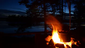 Pot over campfire by lake at dusk.