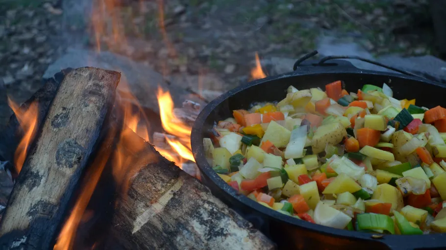 Vegetables cooking in a pot over campfire.