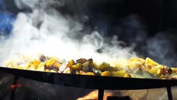 Potatoes frying on a smoky outdoor grill.