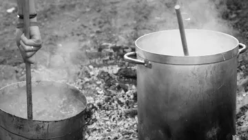 Hand stirring pots over outdoor fire.