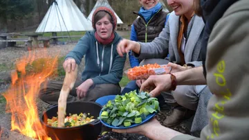 People cooking vegetables over an outdoor fire.