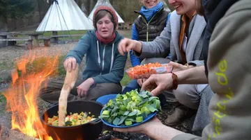 Gruppe kocht Gemüse über Lagerfeuer im Freien.