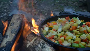 Pfanne mit Gemüse über Lagerfeuer kochen.