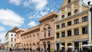 People walking by historic buildings, sunny day.