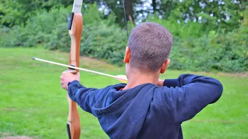 Bogenschütze zielt im Freien auf Grünfläche.