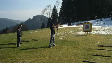 Three people practicing archery in snowy mountains.