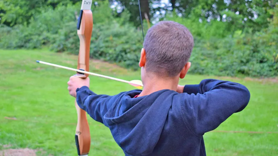 Person aiming a bow in a green field.
