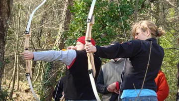 Two people aiming bows in a forest.