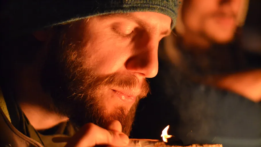 Bearded man lighting a cigarette in the dark.