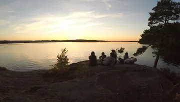Personen sitzen auf Felsen und sehen Sonnenuntergang am See.
