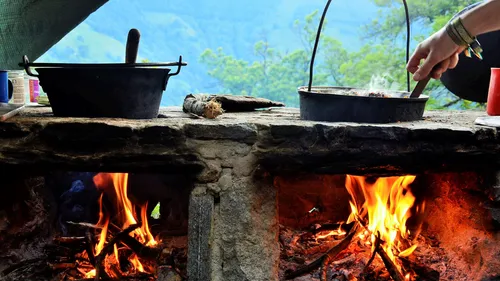 Outdoor stone stove with pots and fire burning.