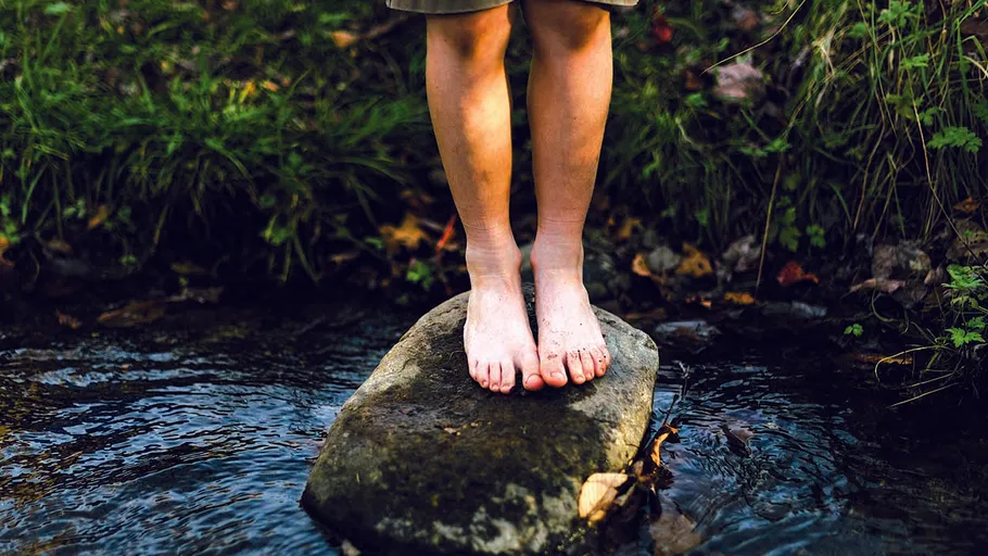 Bare feet standing on rock in stream.