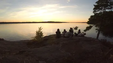 Gruppe sitzt auf Felsen bei Sonnenuntergang am See.