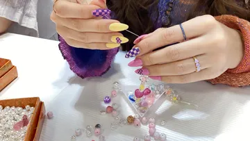 Person stringing beads at a craft table.