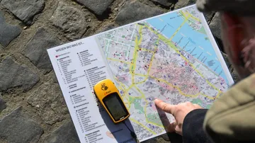Person pointing at map on cobblestone ground.