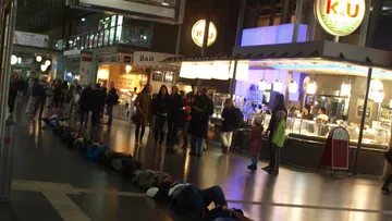 People lying on floor in busy indoor market.