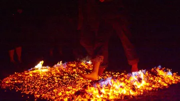 Person walking on glowing hot coals at night.