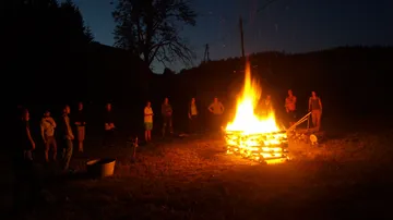Personen versammeln sich um ein großes Lagerfeuer nachts.