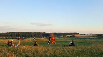 Leute entspannen sich um ein Lagerfeuer auf einer Wiese.