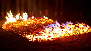 Burning coals with people standing nearby.