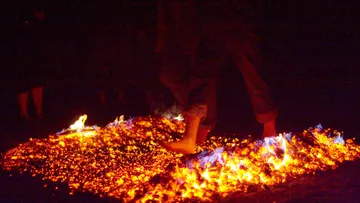 Person walks barefoot on burning coals outdoors.