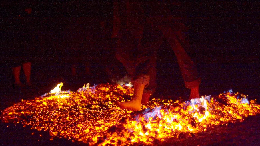 Person walks barefoot on burning coals outdoors.