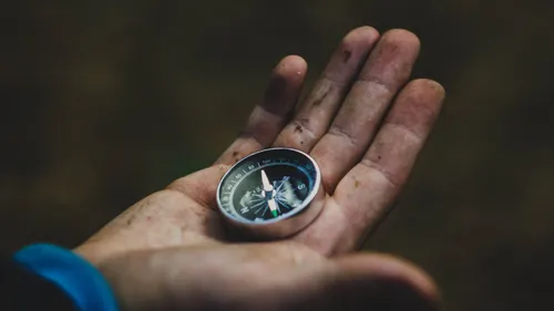 Hand holding compass, outdoor setting.