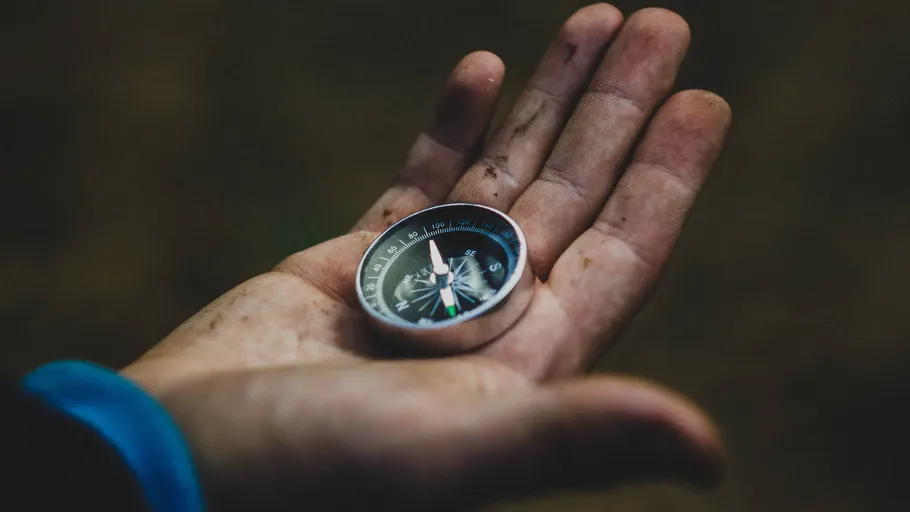 Compass rests in a dirty hand outdoors.