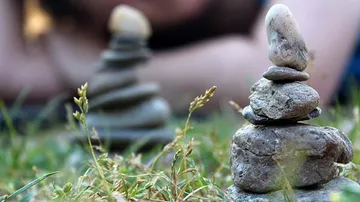 Stacked stones on grass with blurred person.