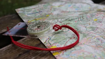 Compass resting on a colorful map outdoors.