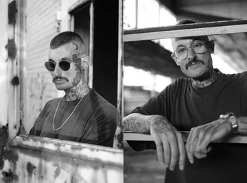 Mann mit Tattoos posiert in industrieller Umgebung.