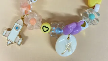 Buntes Armband mit Anhängern auf beigem Hintergrund.