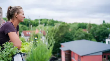 Frau auf Balkon blickt auf grüne Landschaft.