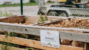 Kompostbehälter mit Schild in Gartenszene.
