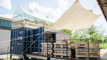 Versandcontainer-Gewächshaus mit Sitzbereich.