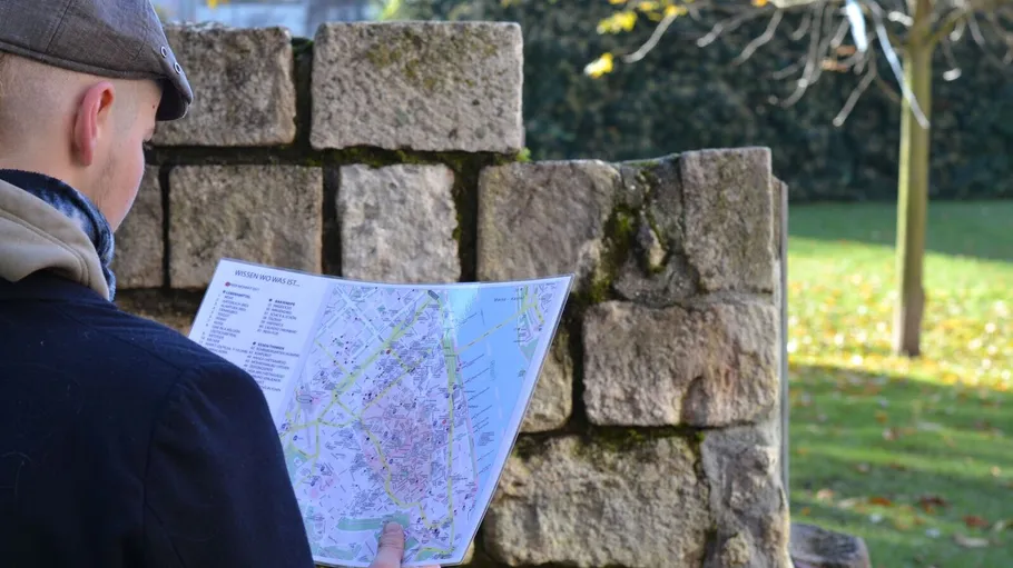 Person reading a map by stone wall.