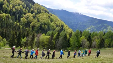 People holding hands, walking in mountainous forest.