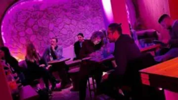 People seated at tables in a purple-lit room.