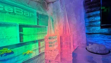 Ice sculpture of cathedral in colorful lit room.