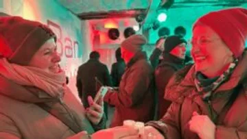 Two people in winter clothes sharing a drink.