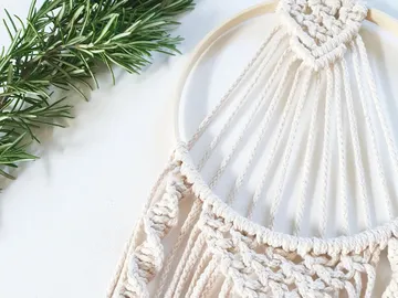 Macrame hanger features ornate knots surrounded by green leaves